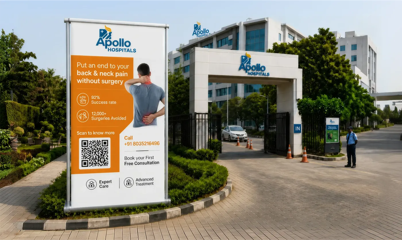 An Apollo Hospitals banner at a hospital entrance gate promoting non-surgical back and neck pain treatment, with a 'Scan to know more' QR Code