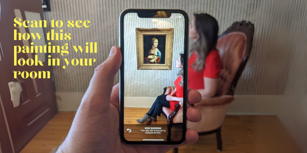 A hand holding a smartphone with text "Scan to see how this painting will look in your room"